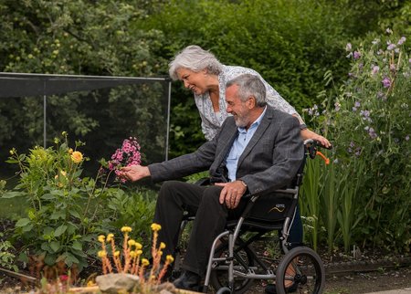 Ein Rollstuhlfahrer und seine Frau erkunden verschiedene Pflanzen in einem Garten